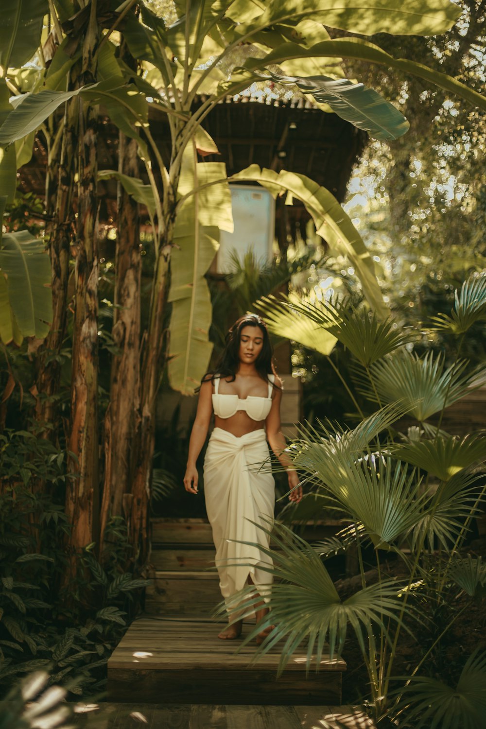 woman in white spaghetti strap top and brown and white plaid skirt standing near palm tree