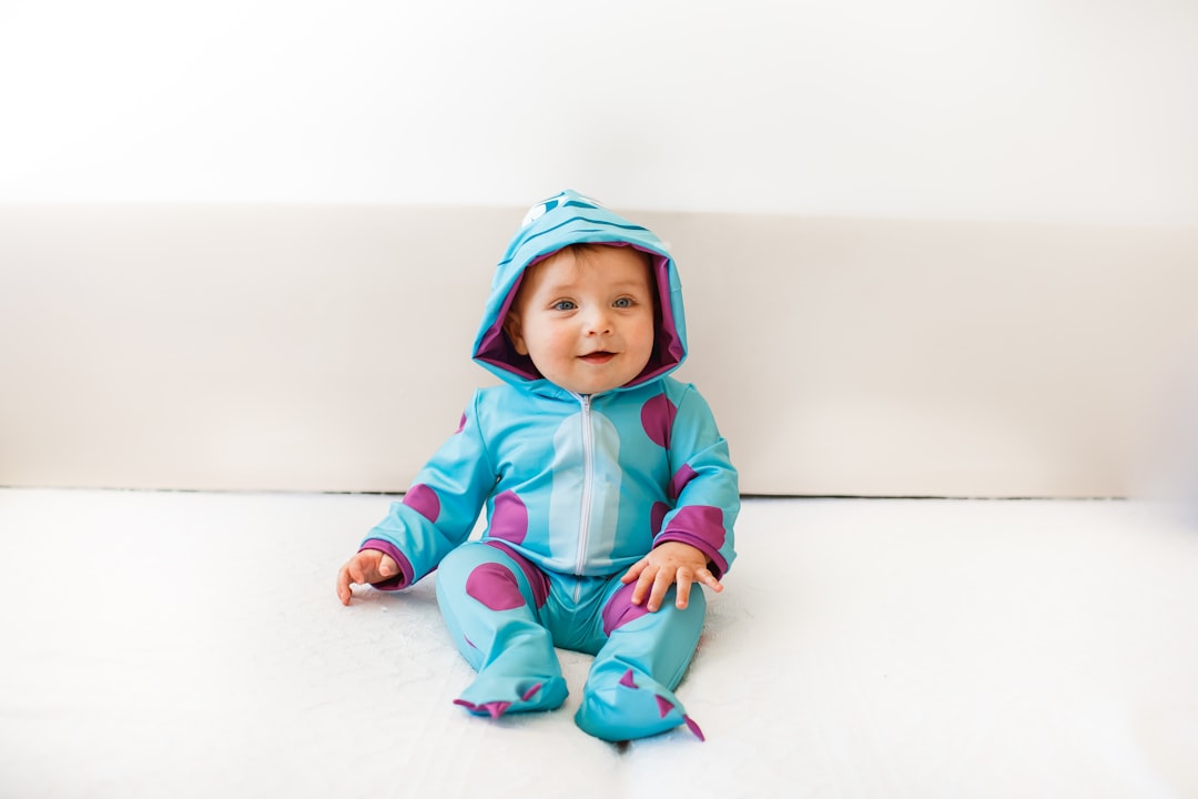 girl in pink hoodie and blue pants sitting on white floor