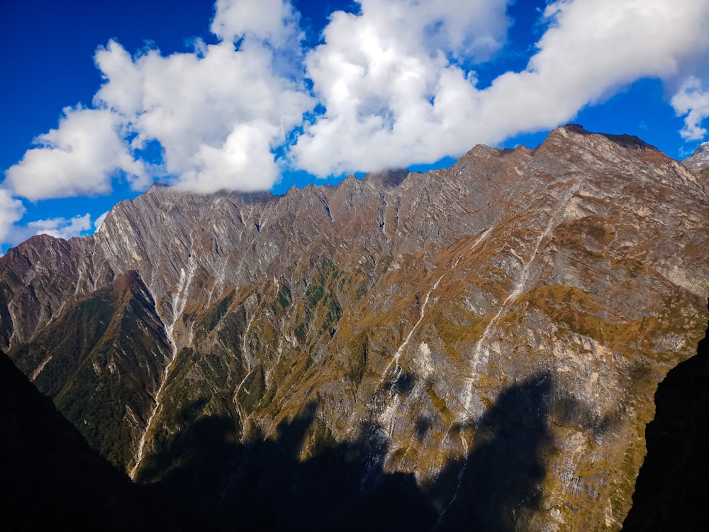 green trees on brown mountain under white clouds and blue sky during daytime