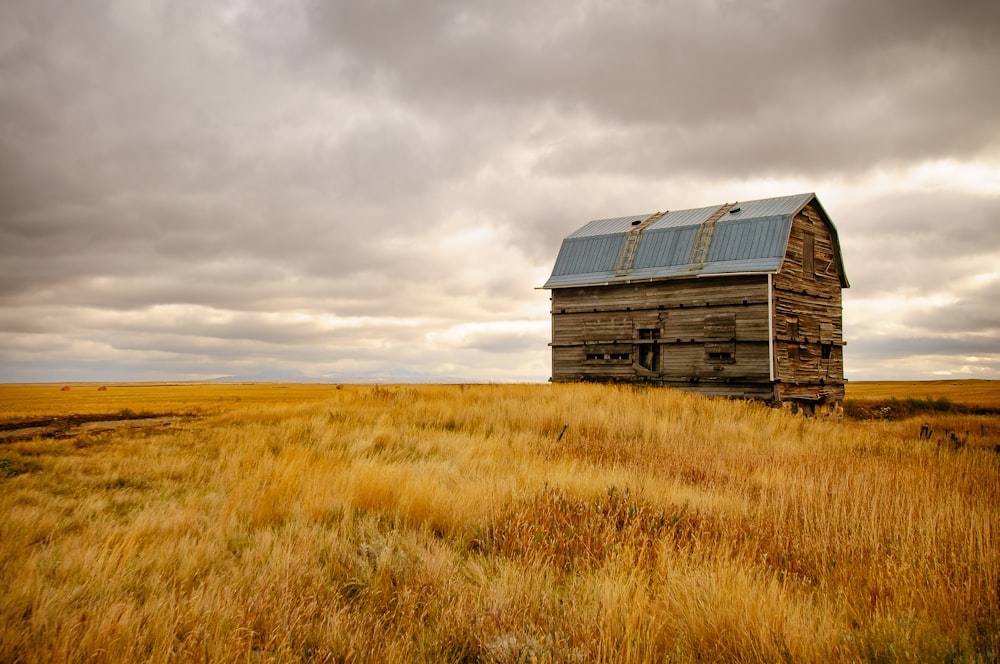 casa de madeira marrom no campo de grama marrom sob nuvens cinzentas