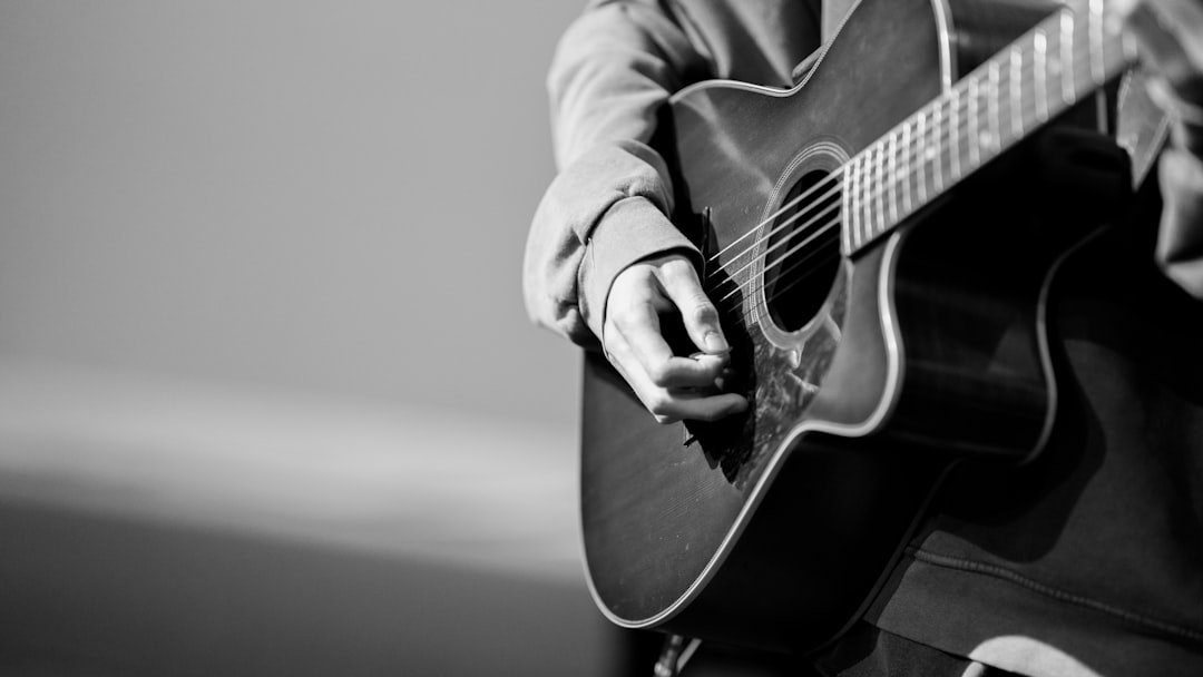 person playing acoustic guitar in grayscale photography