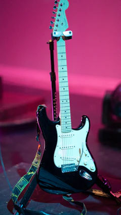 Vibrant electric guitar resting on a stand with colorful stage lights in the background.