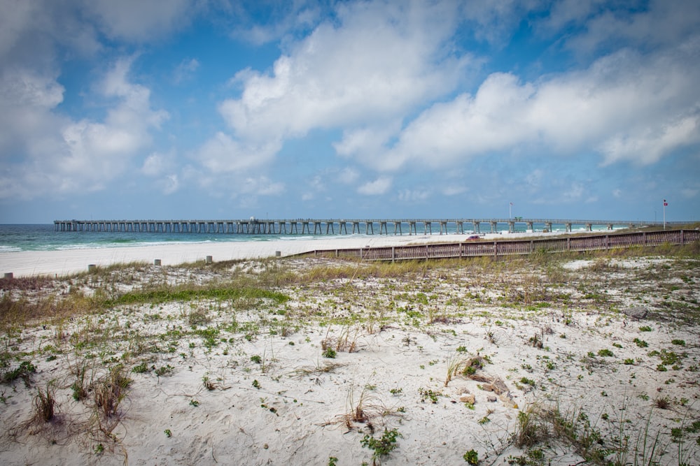 white sand beach with bridge under blue sky and white clouds during daytime
