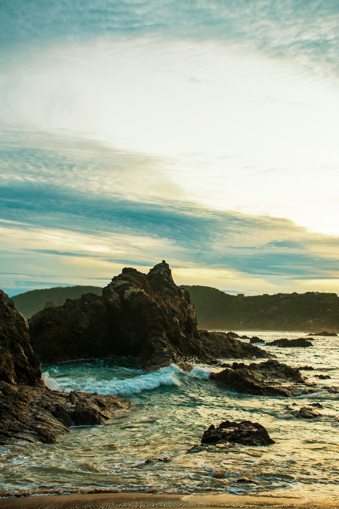 black rock formation on body of water under white clouds and blue sky during daytime