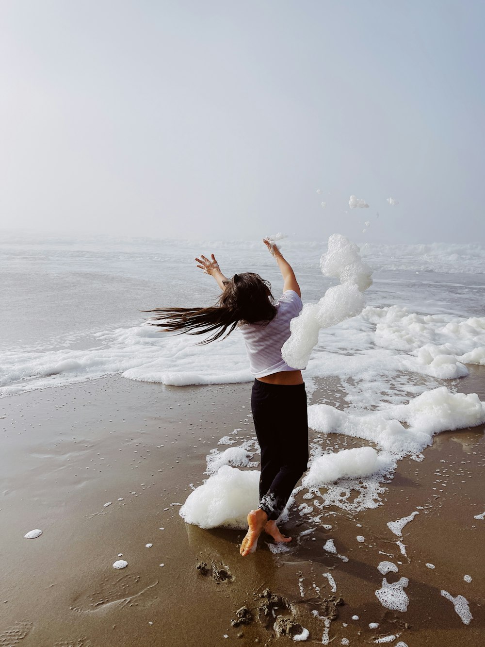 woman in black pants standing on white snow near body of water during daytime