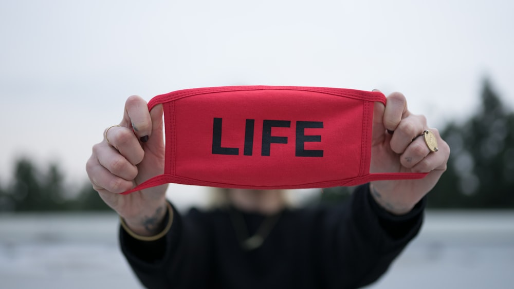 a person holding up a red hat with the word life printed on it