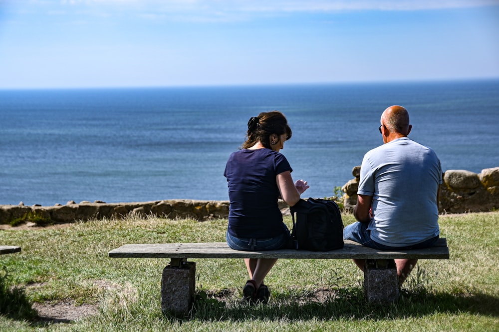 casal sentado no banco perto do mar durante o dia