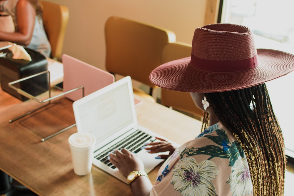 woman in green and white floral long sleeve shirt wearing brown fedora hat sitting on orange