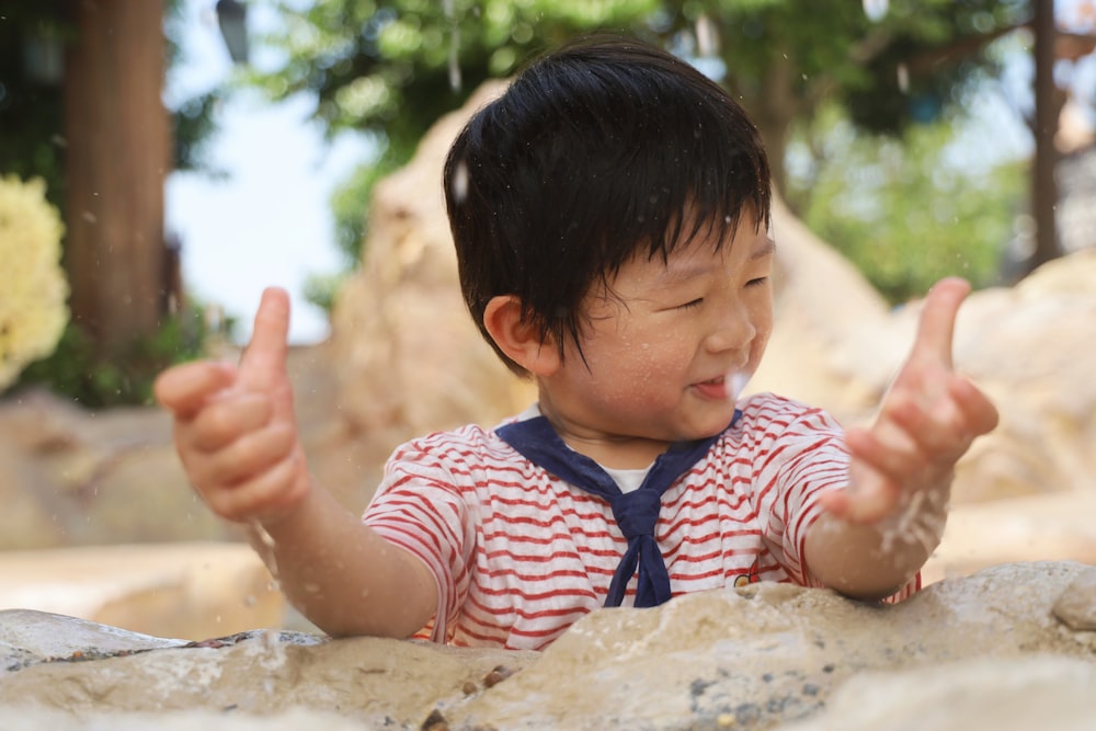 昼間、砂の上に座る赤と白のストライプのシャツを着た女の子