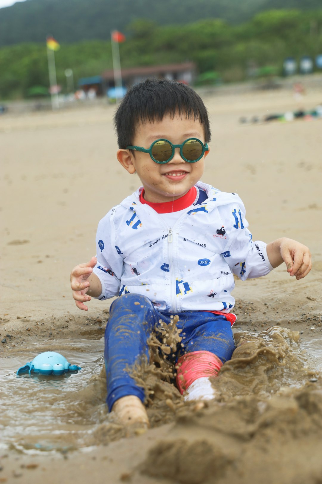 boy in white and blue star print polo shirt and brown pants sitting on brown sand
