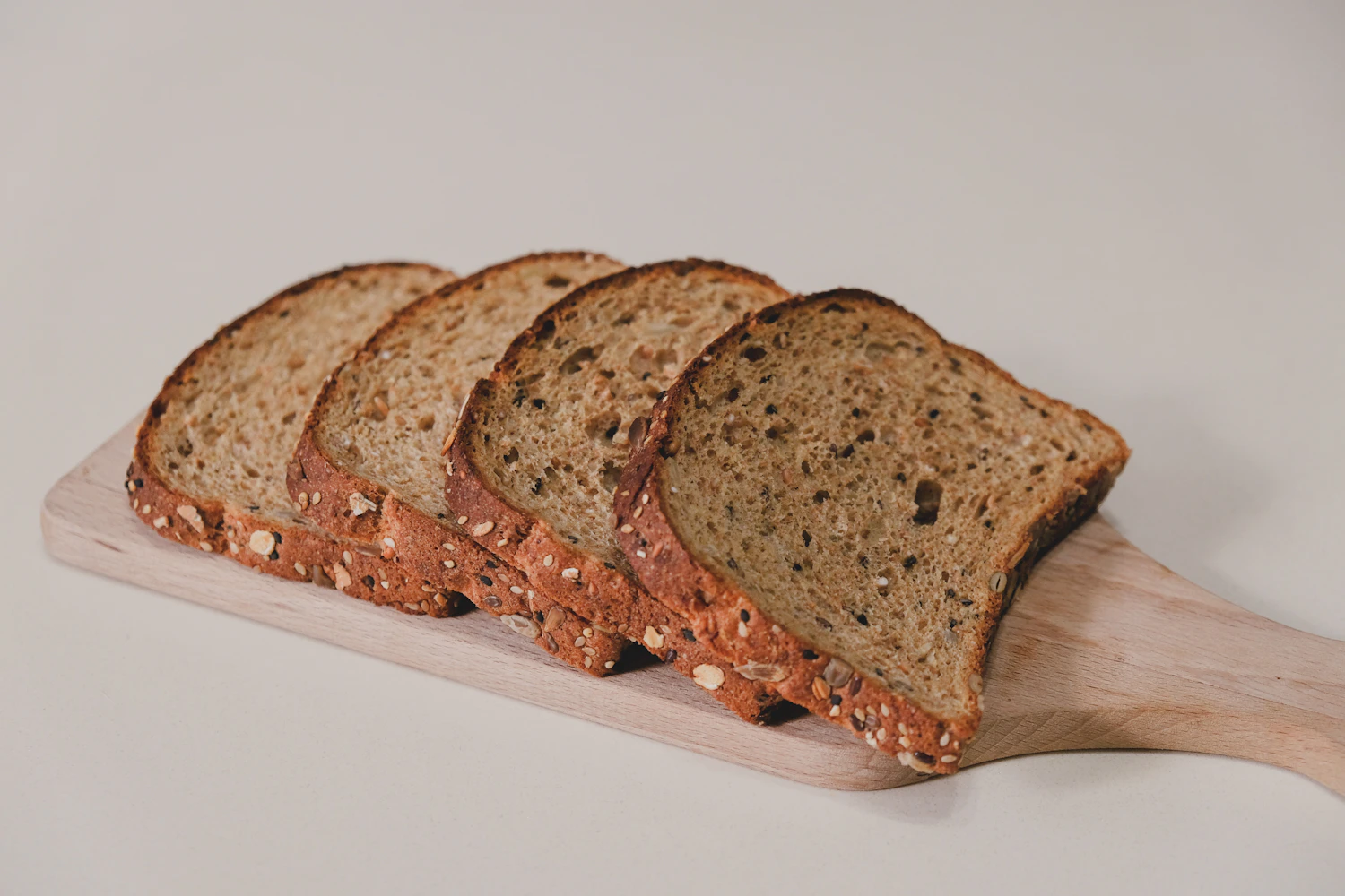 Four seeded slices fanned out on a wooden paddle against a pale ground