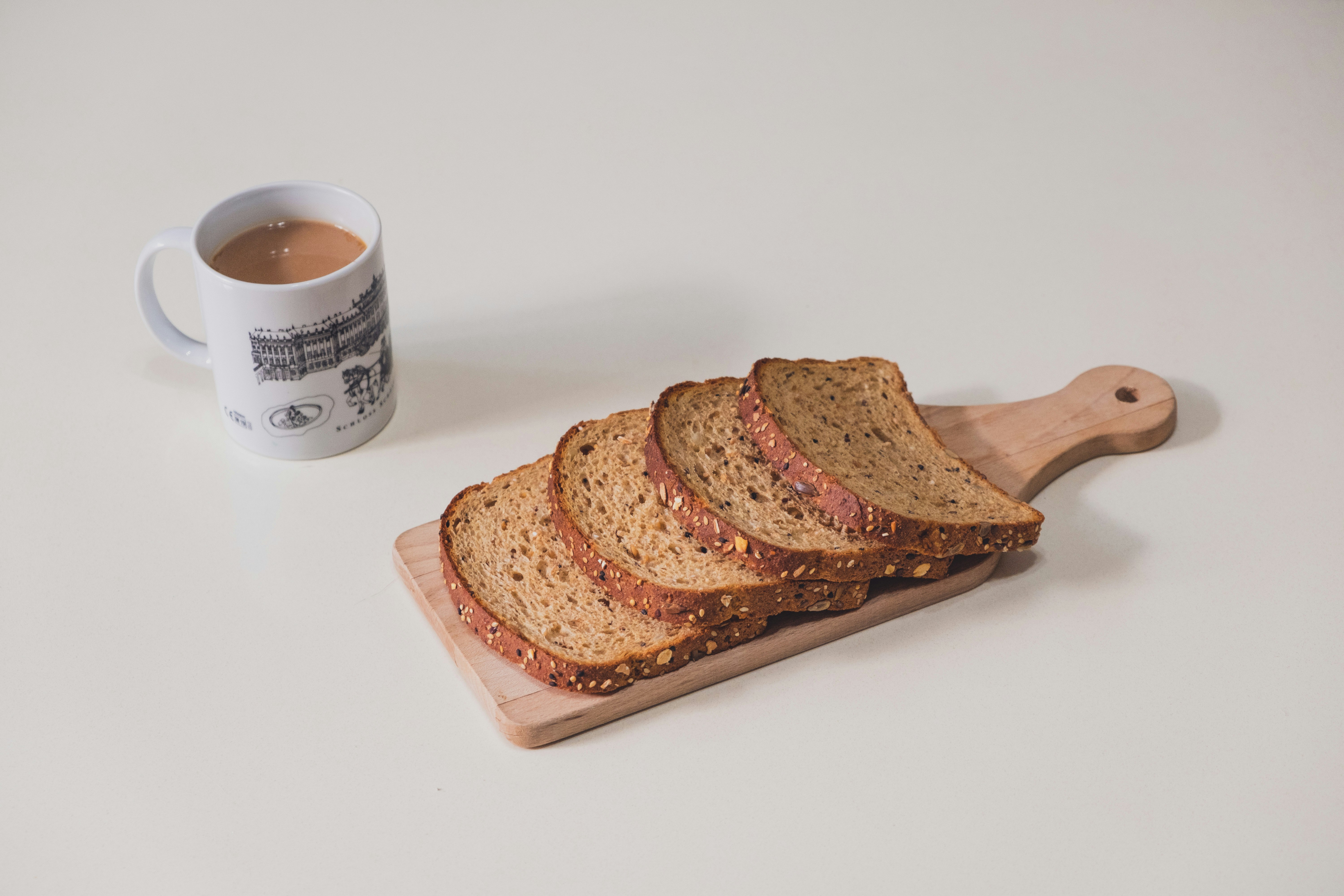 sliced bread on brown wooden chopping board beside white ceramic mug