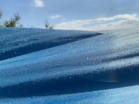 Close-up of a blue tarpaulin fabric with water droplets highlighting its waterproof feature.