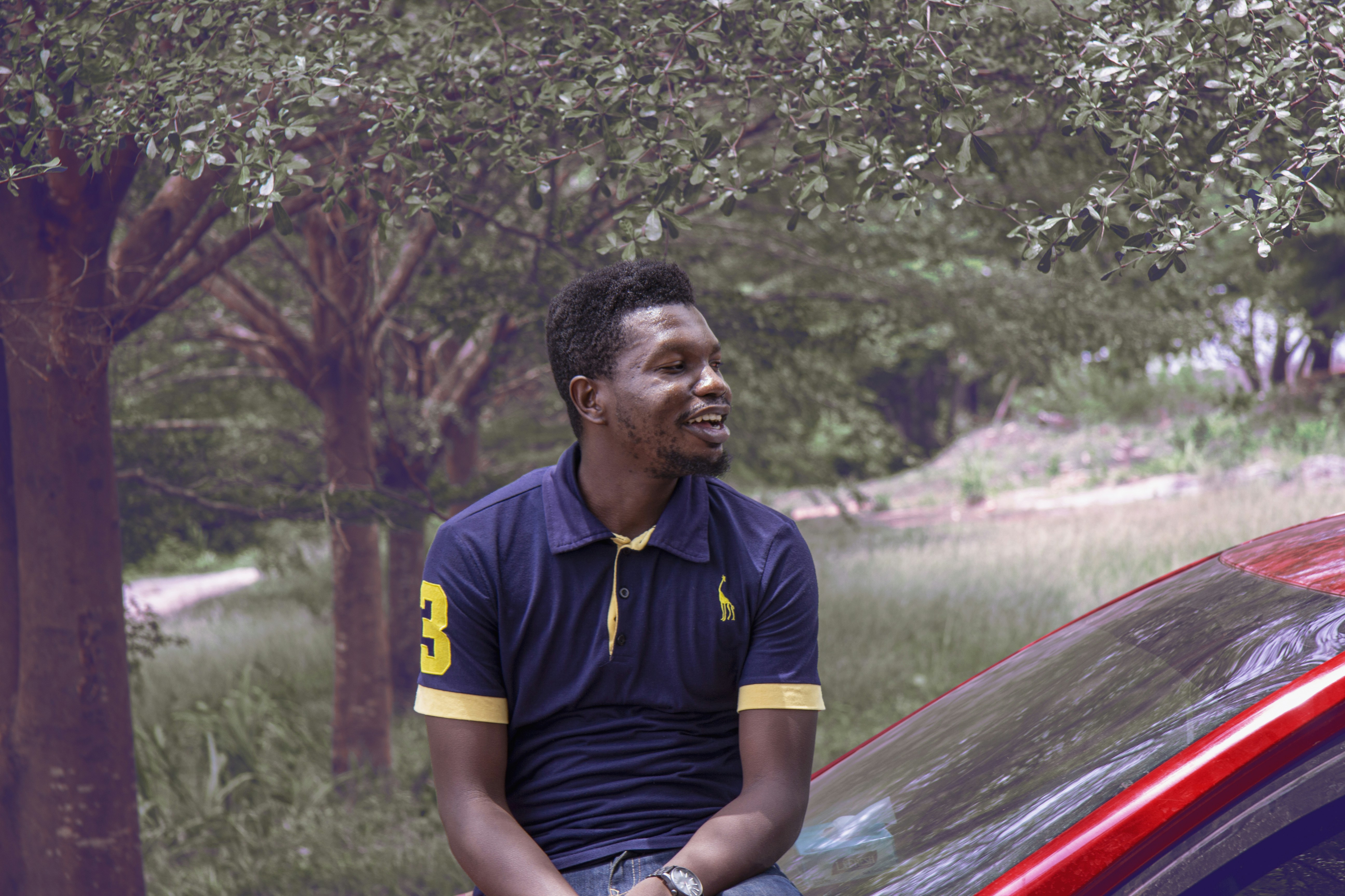 man in black and yellow adidas polo shirt sitting on red car