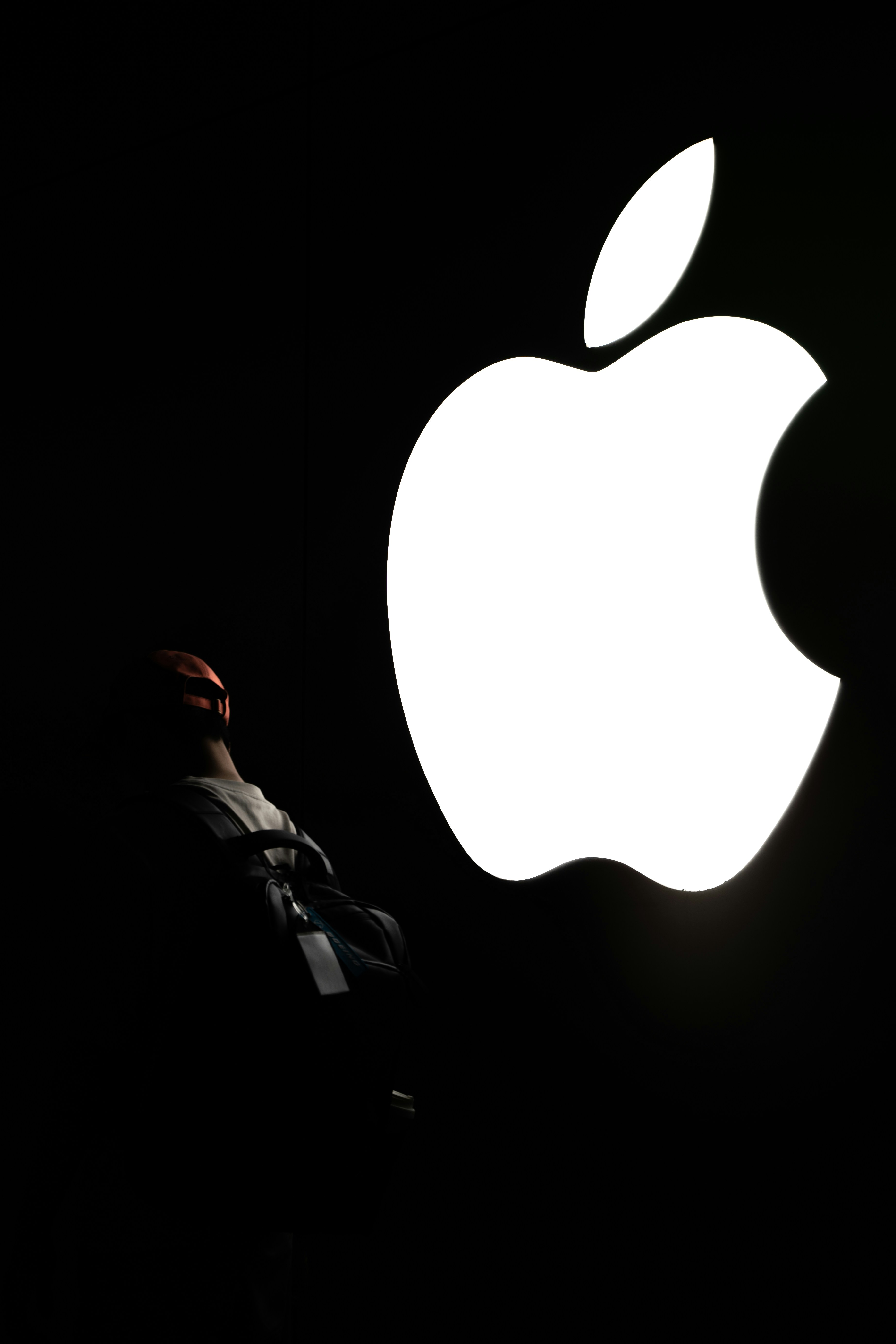 A man walking in front of the Apple Store logo at night in Osaka, Japan.