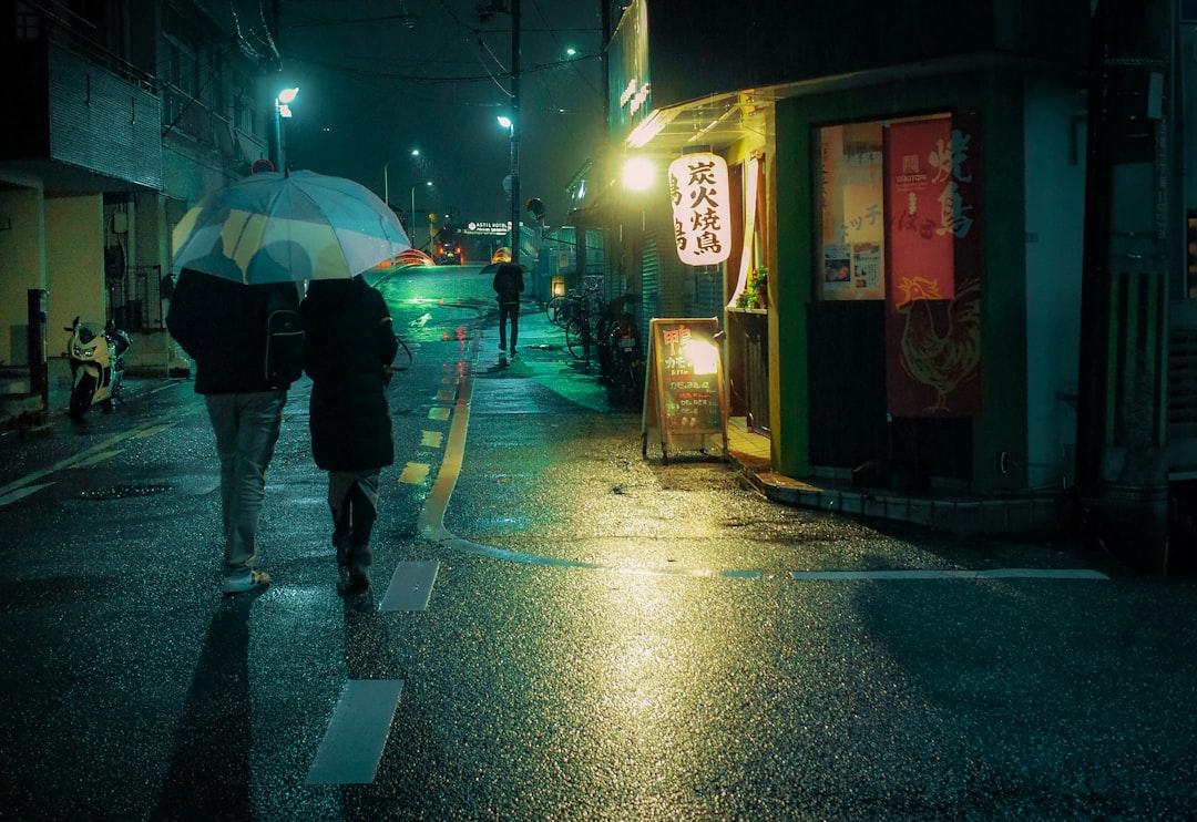 person in black jacket and black pants holding umbrella walking on sidewalk during night time