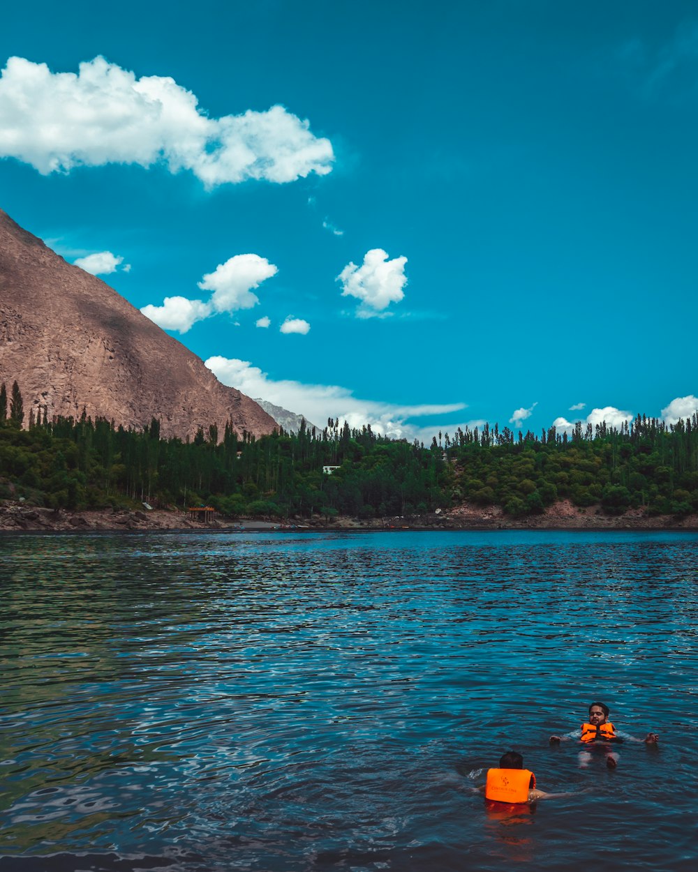 昼間、青空の下、山の近くの湖でカヤックに乗る人々
