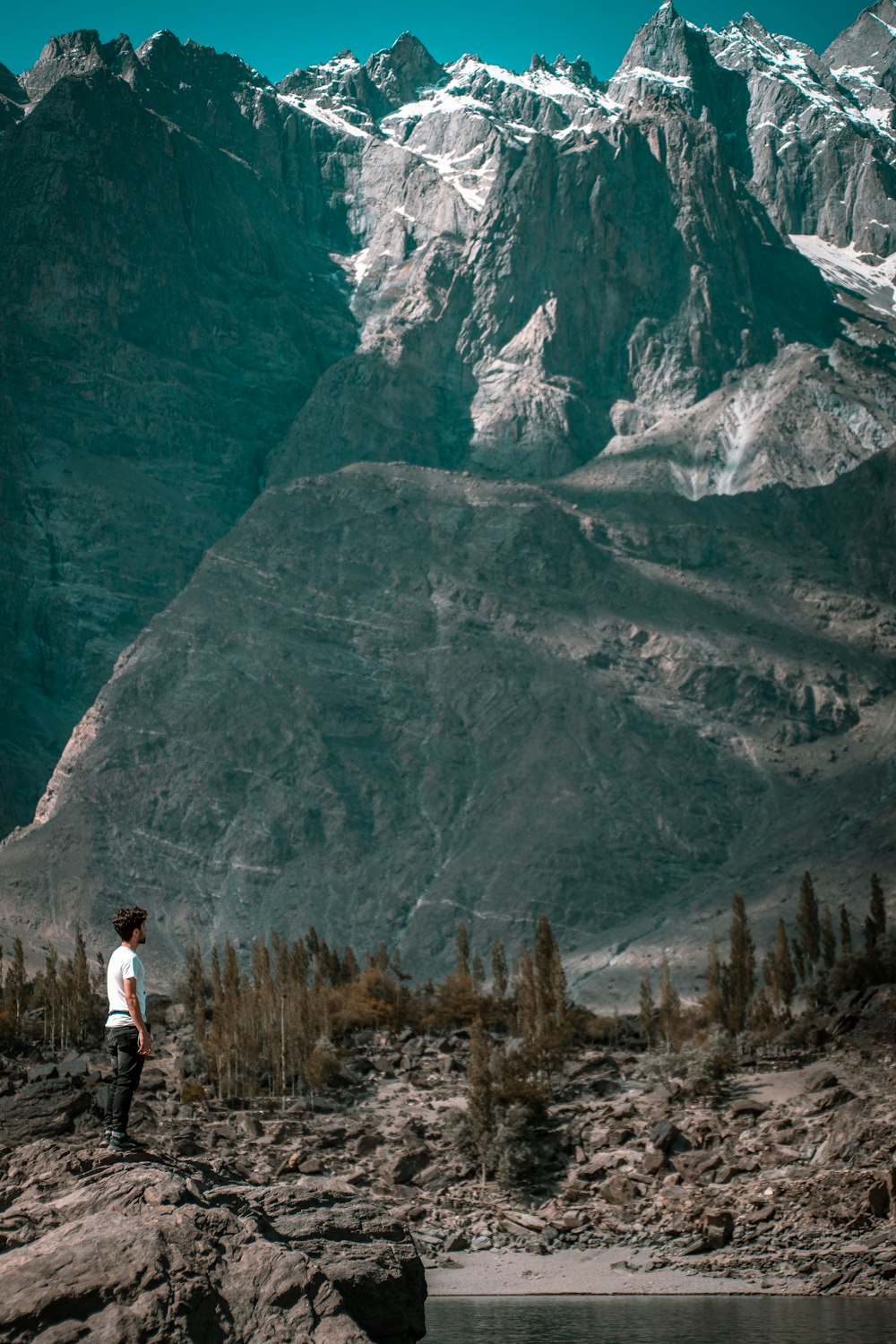 uomo in camicia bianca in piedi sull'erba marrone vicino alla montagna durante il giorno