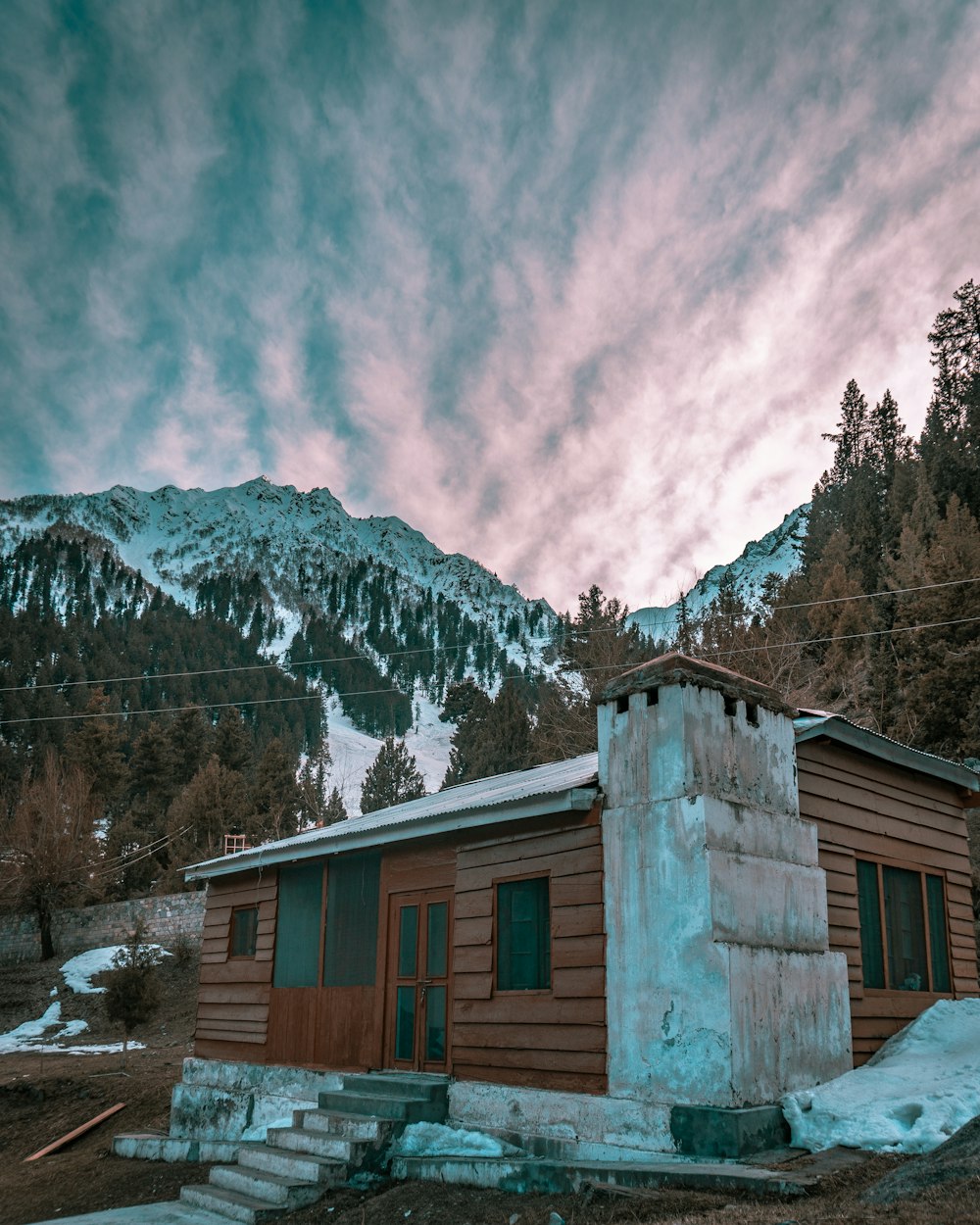 brown wooden house near snow covered mountain under cloudy sky during daytime
