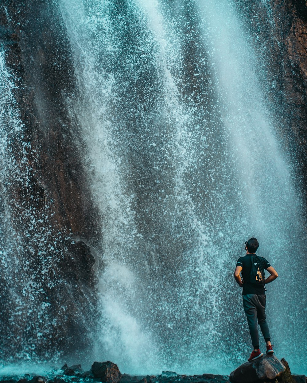 man in black jacket and black pants standing in front of water falls