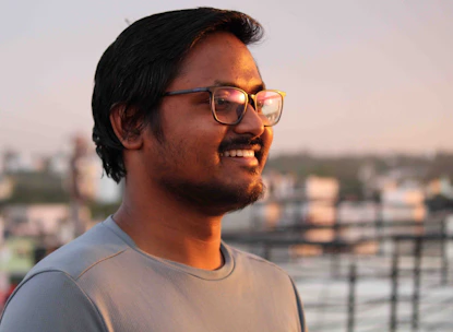 A stylish person wearing sleek rectangular glasses, smiling outdoors in a city setting.