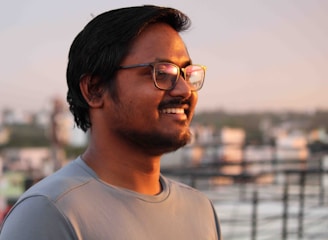 A smiling person wearing oil-resistant eyeglasses outdoors, with a blurred cityscape background.