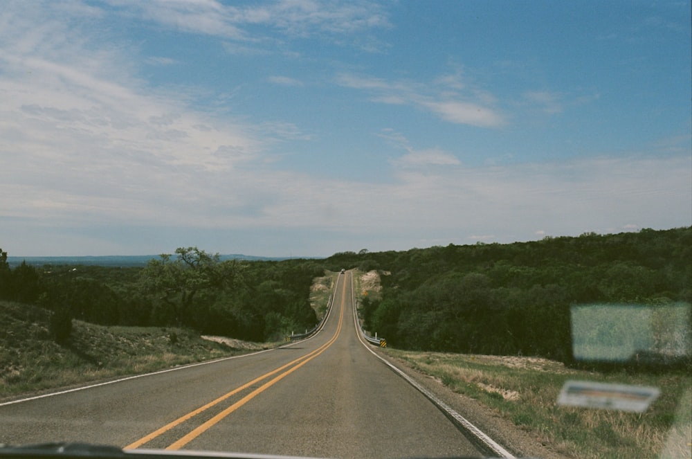 gray concrete road between green trees under blue sky during daytime