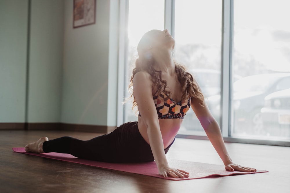 donna in reggiseno floreale bianco e nero e pantaloni neri in ginocchio sul tappetino da yoga rosa