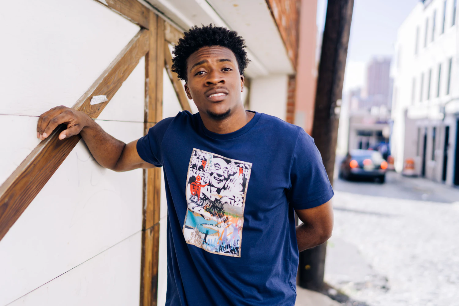 The Boxy Tee in ink, worn with the printed panel, against a side-street wall