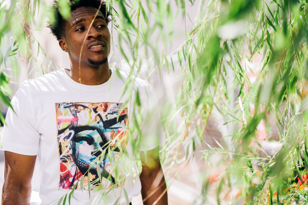 man in white crew neck t-shirt standing beside green plants during daytime