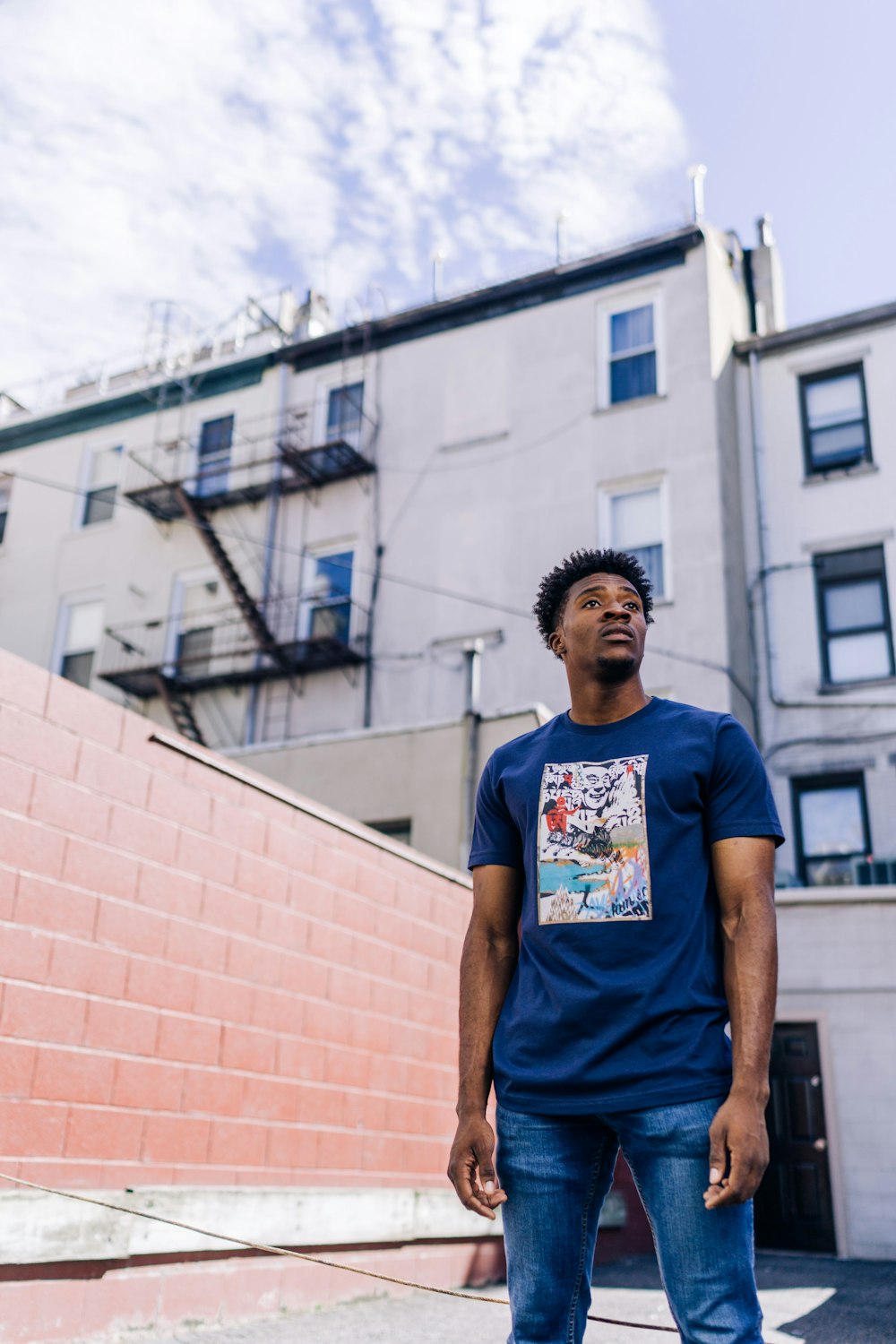man in blue crew neck t-shirt standing near brown concrete building during daytime