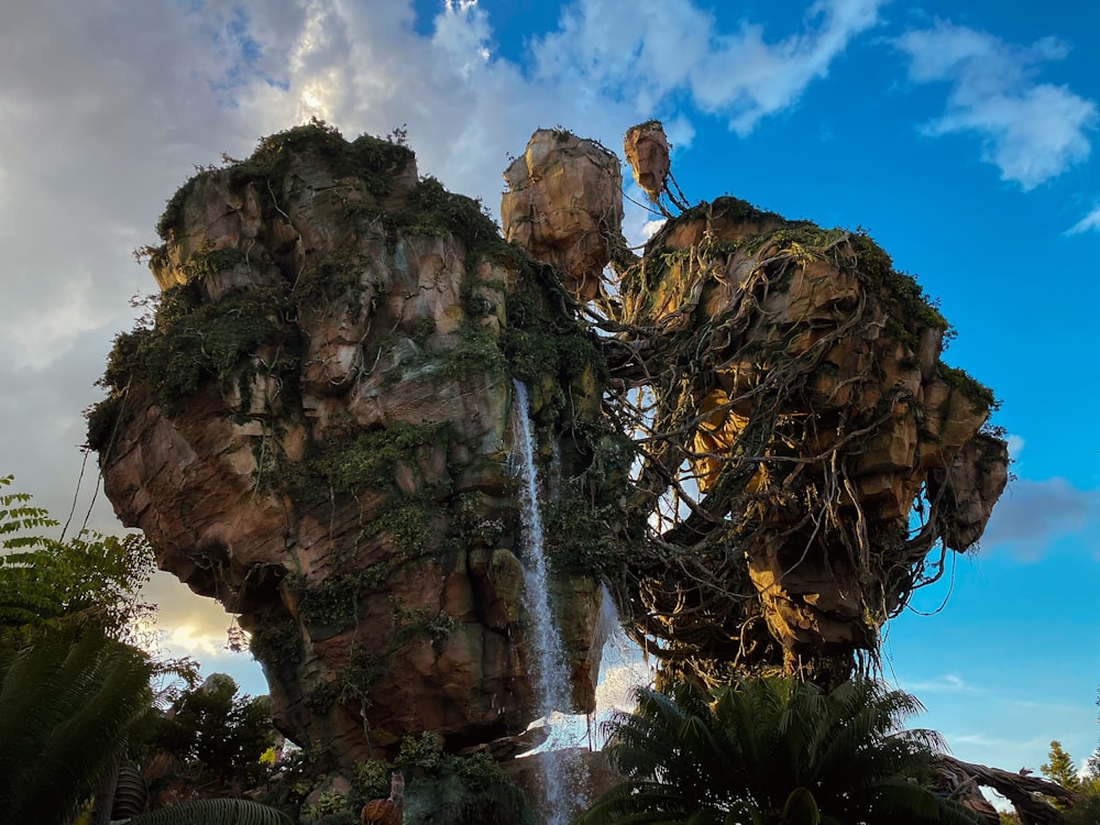 brown rock formation with water falls under blue sky and white clouds during daytime