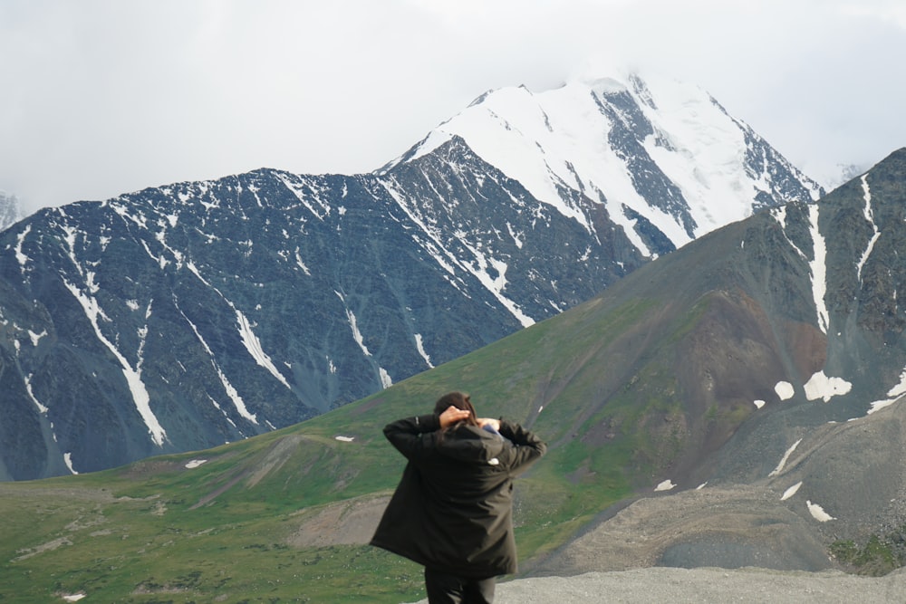 man in black jacket sitting on green grass field near snow covered mountain during daytime