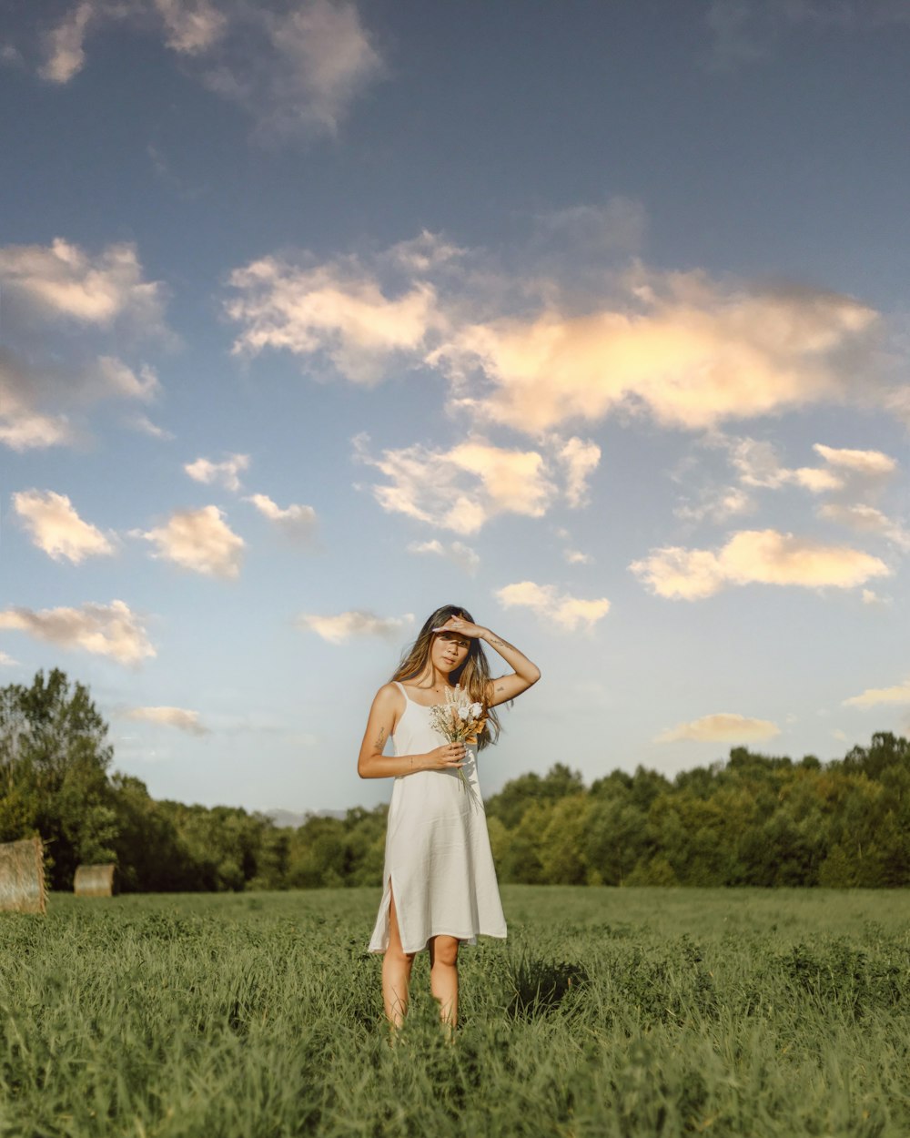 woman in white dress standing on green grass field under blue and white cloudy sky during