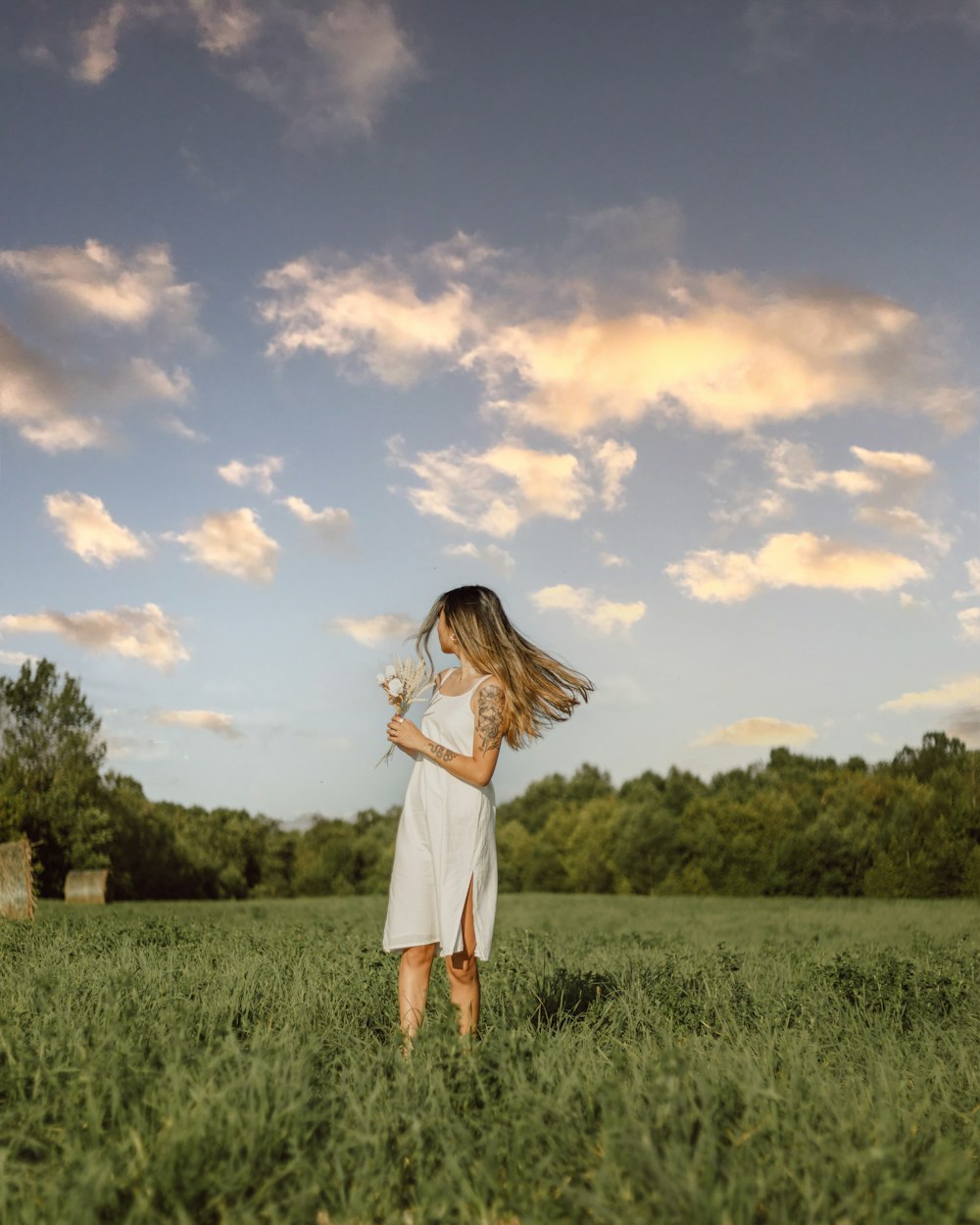 woman in white dress standing on green grass field under blue and white cloudy sky during