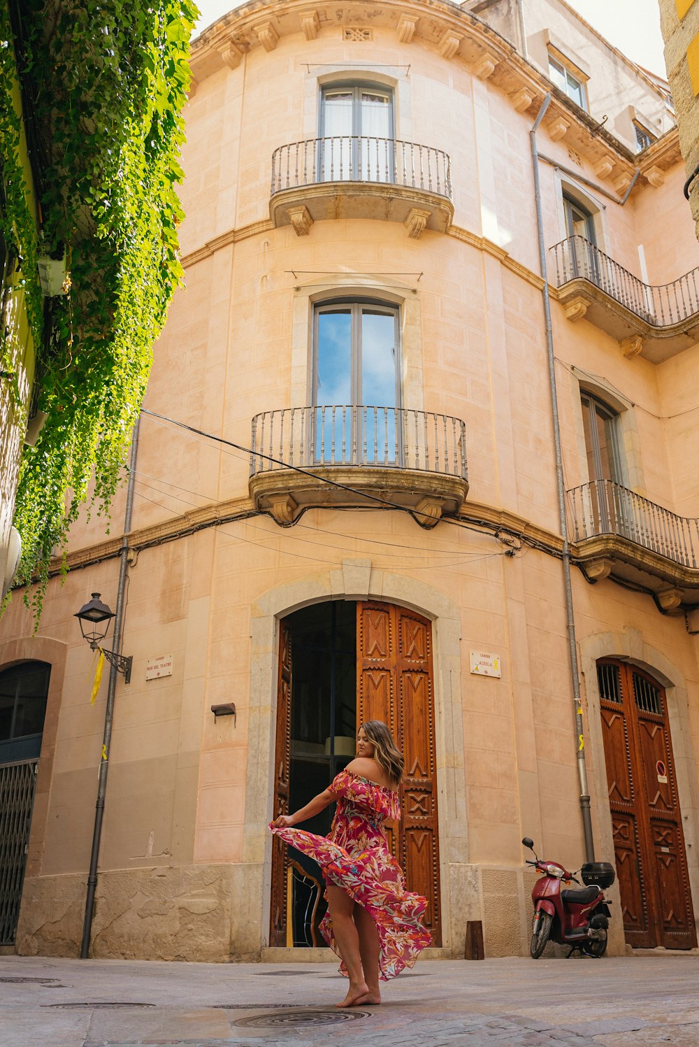 woman in red and white floral dress standing in front of beige concrete building during daytime