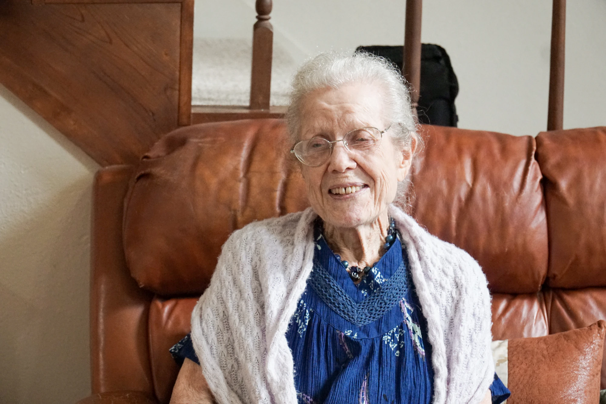 An older woman smiling as she sits on a sofa at home