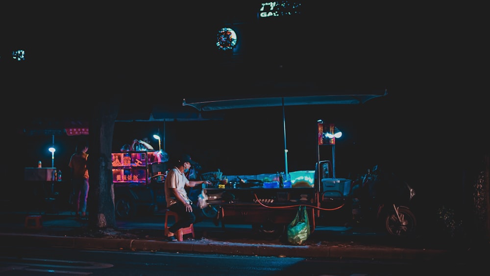 man in white t-shirt and black pants sitting on black metal bench during nighttime