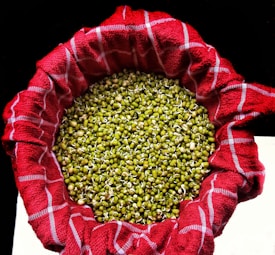 A large quantity of green mung bean sprouts resting inside a bowl lined with a red checkered cloth. The sprouts are densely packed and display small white shoots emerging from the beans.