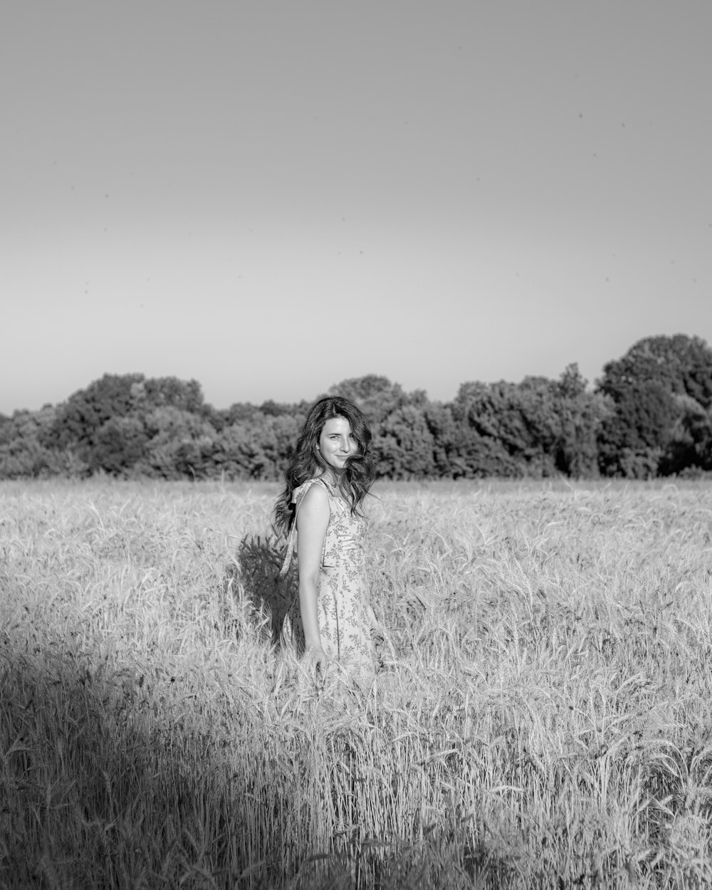 grayscale photo of woman in white dress standing on grass field