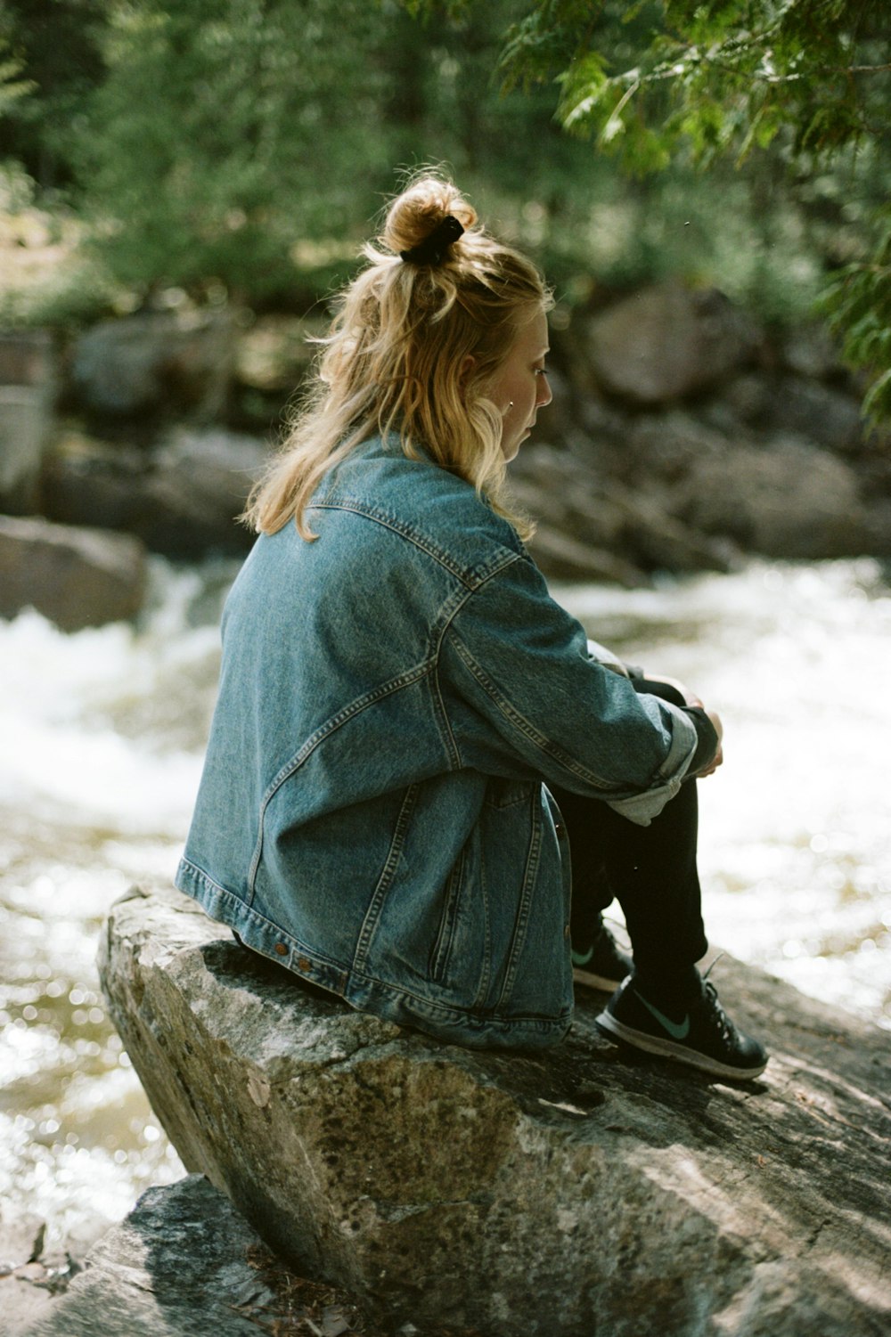 woman in blue denim jacket sitting on rock during daytime