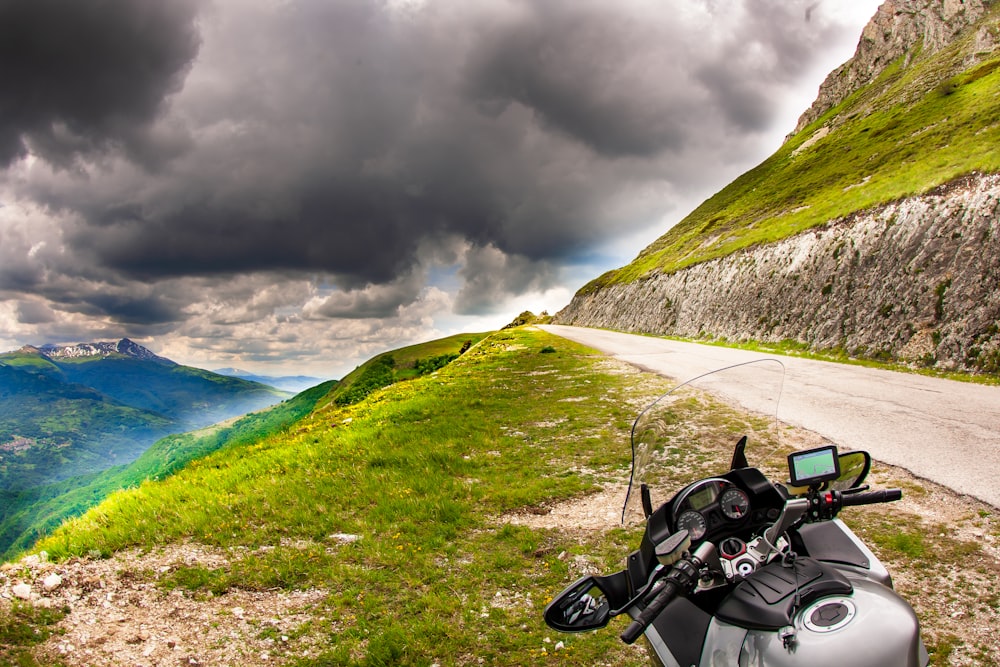 black motorcycle on green grass field near mountain under cloudy sky during daytime