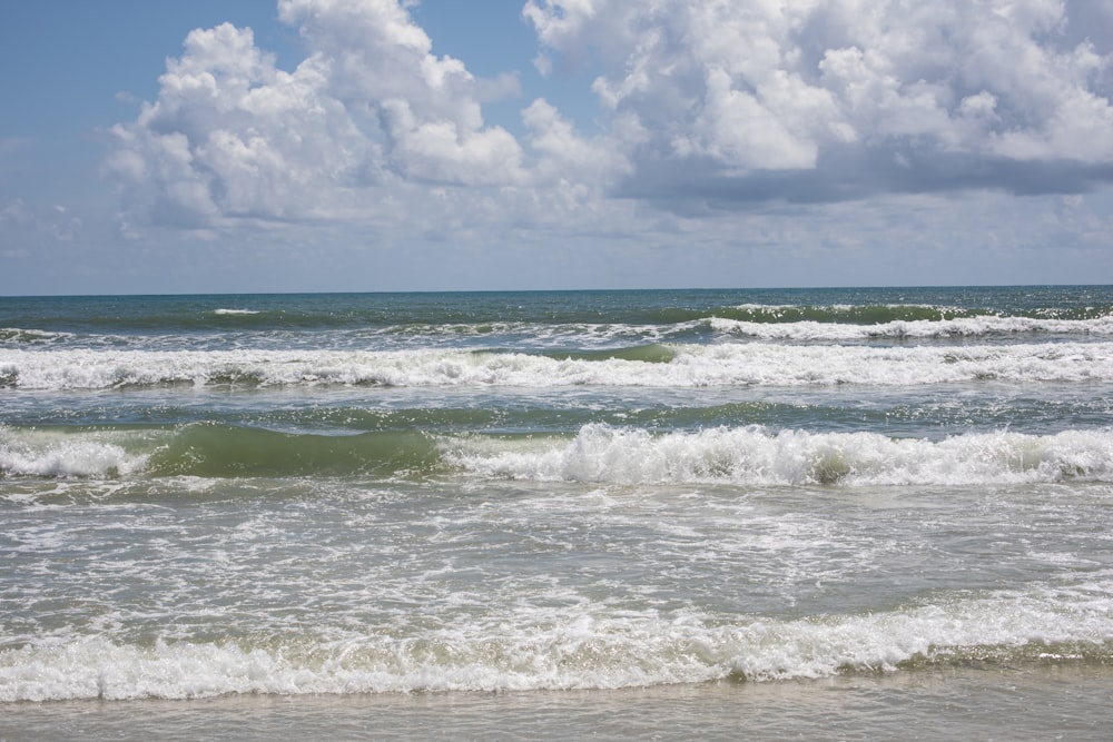 ocean waves under white clouds and blue sky during daytime