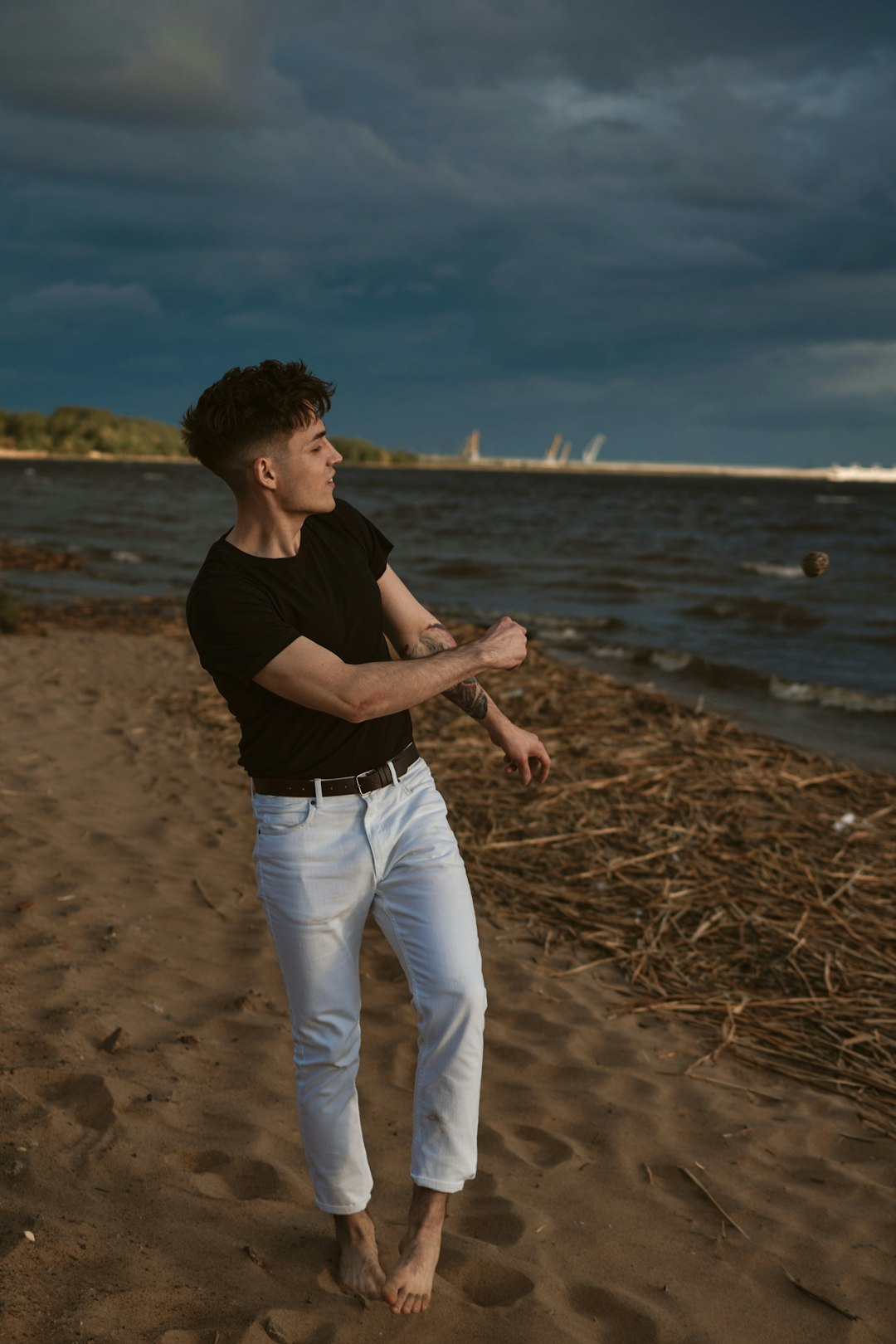 man in black t-shirt and white pants standing on brown sand during daytime