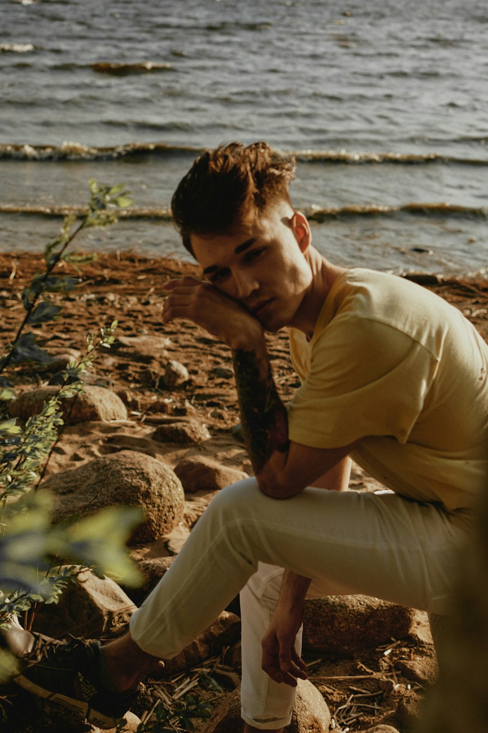 man in brown shirt and white pants sitting on rock near body of water during daytime