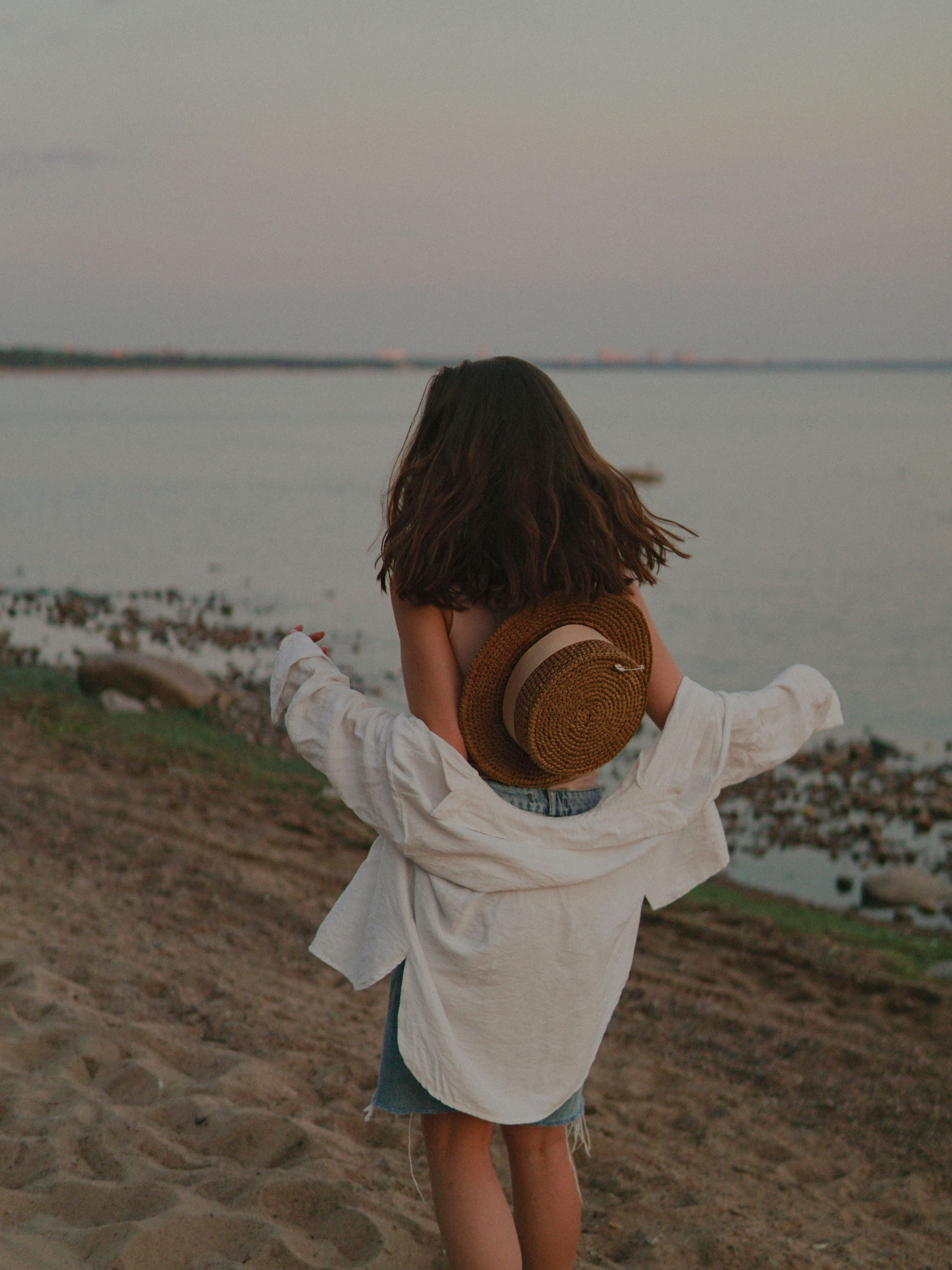 Femme en chemise blanche à manches longues tenant un chapeau marron debout sur le sable brun pendant la journée