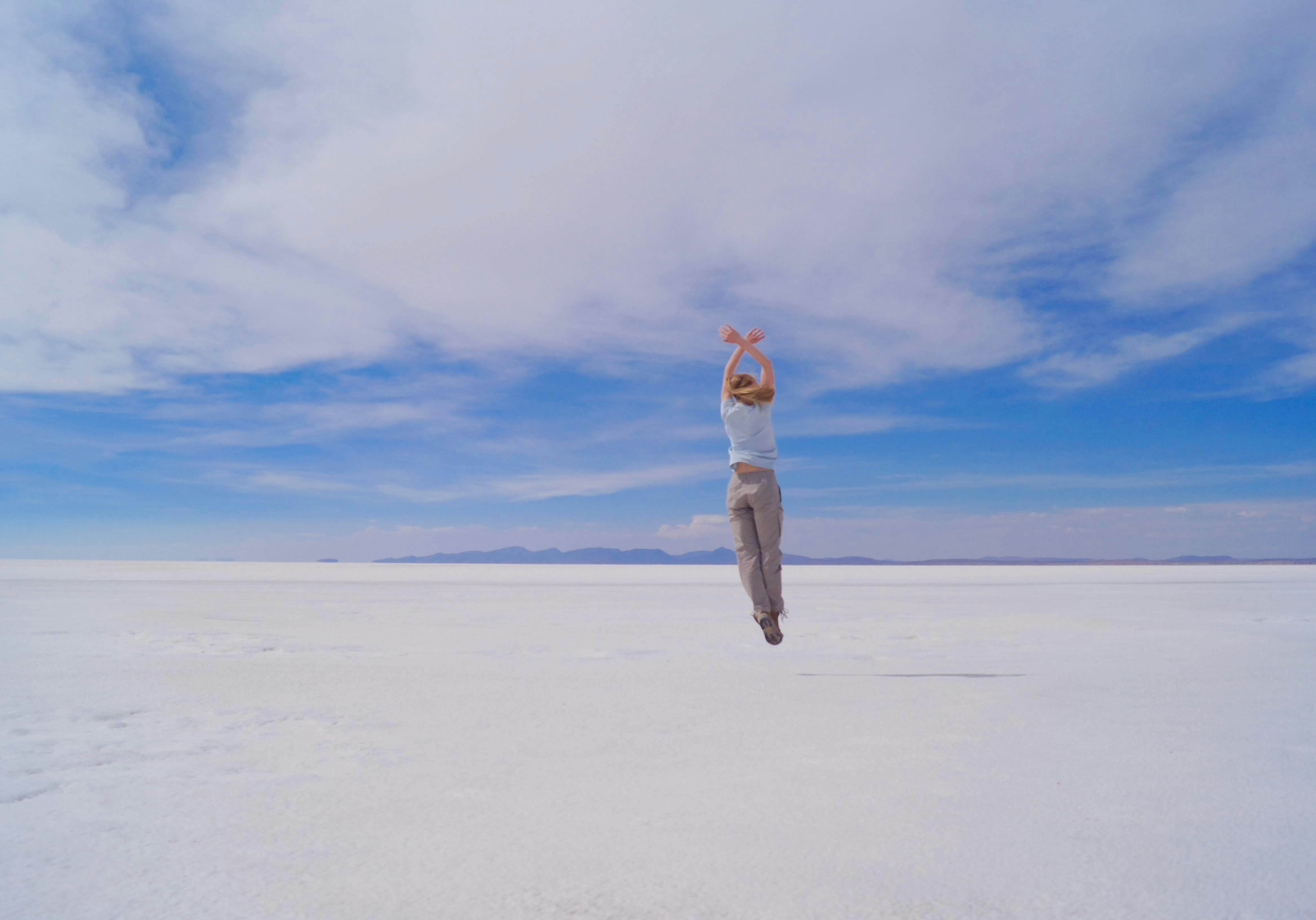 woman in white jacket and gray pants standing on white sand under blue sky during daytime