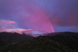 A vibrant rainbow arching over a serene landscape at sunset.