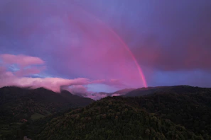 A vibrant rainbow arching over a serene landscape at sunset.