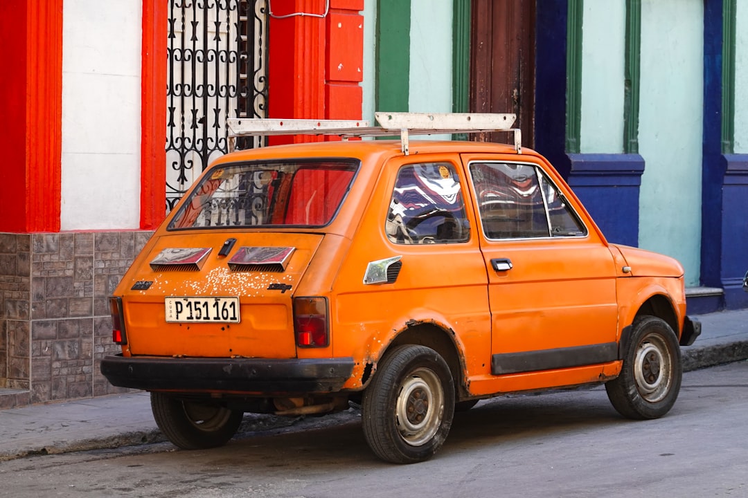 orange 5 door hatchback parked beside red and white building during daytime